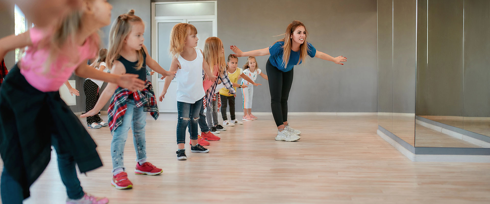 Happy boys and girls doing stretching exercises with female dance teacher in the dance studio. Choreography concept